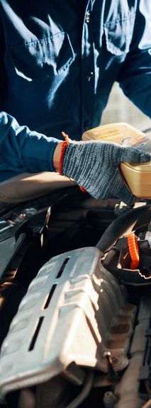 Behandschuhte Hände des Mechanikers, der hochwertiges Öl in den Motor im Auto gießt